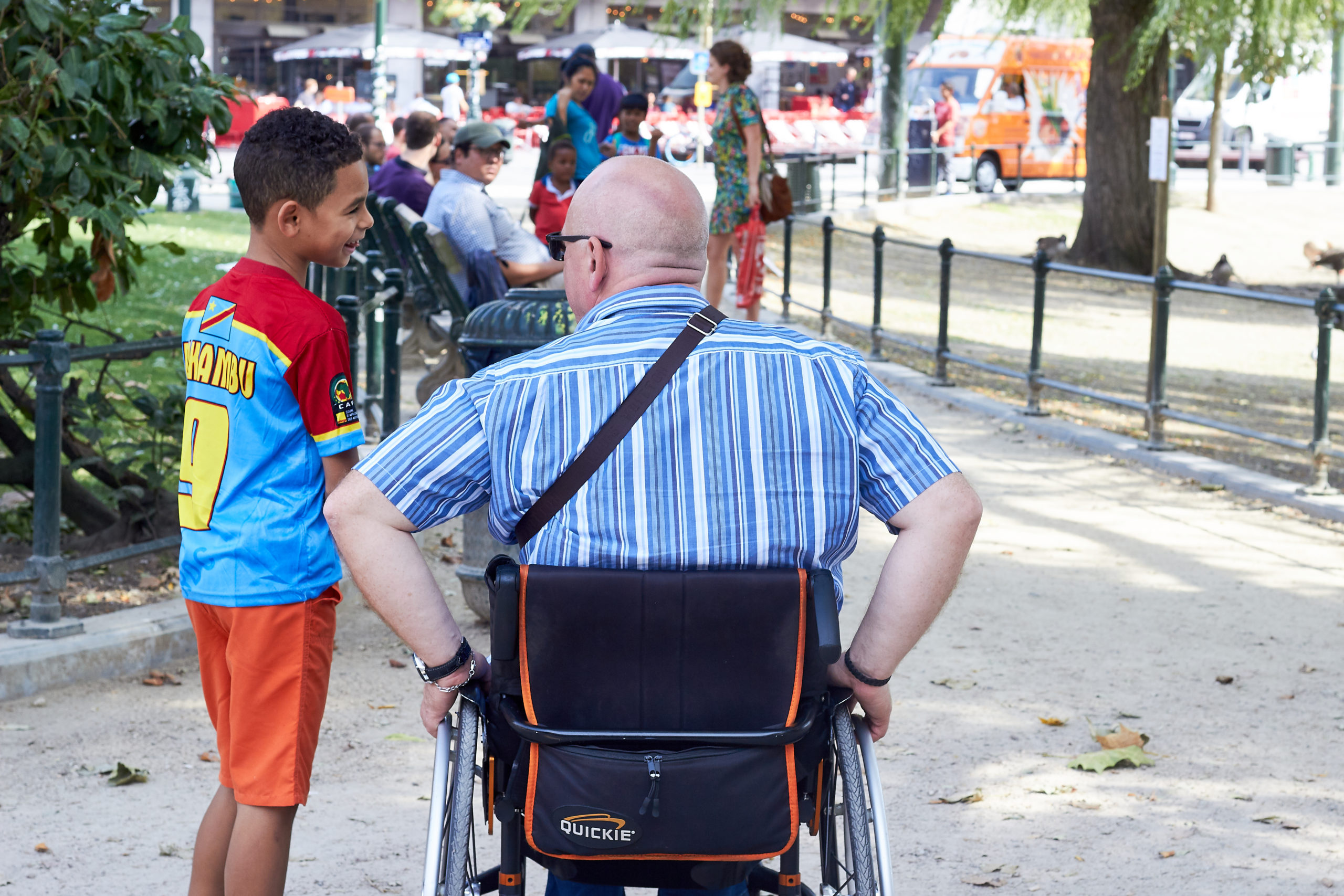 Personne à mobilité réduite dans une chaise roulante de dos discutant avec un jeune garçon