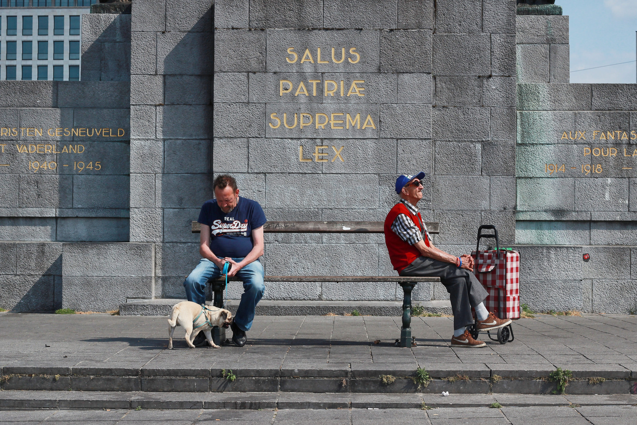 Deux hommes assis chacun à l'extrémité d'un banc et l'un tient un chien en laisse