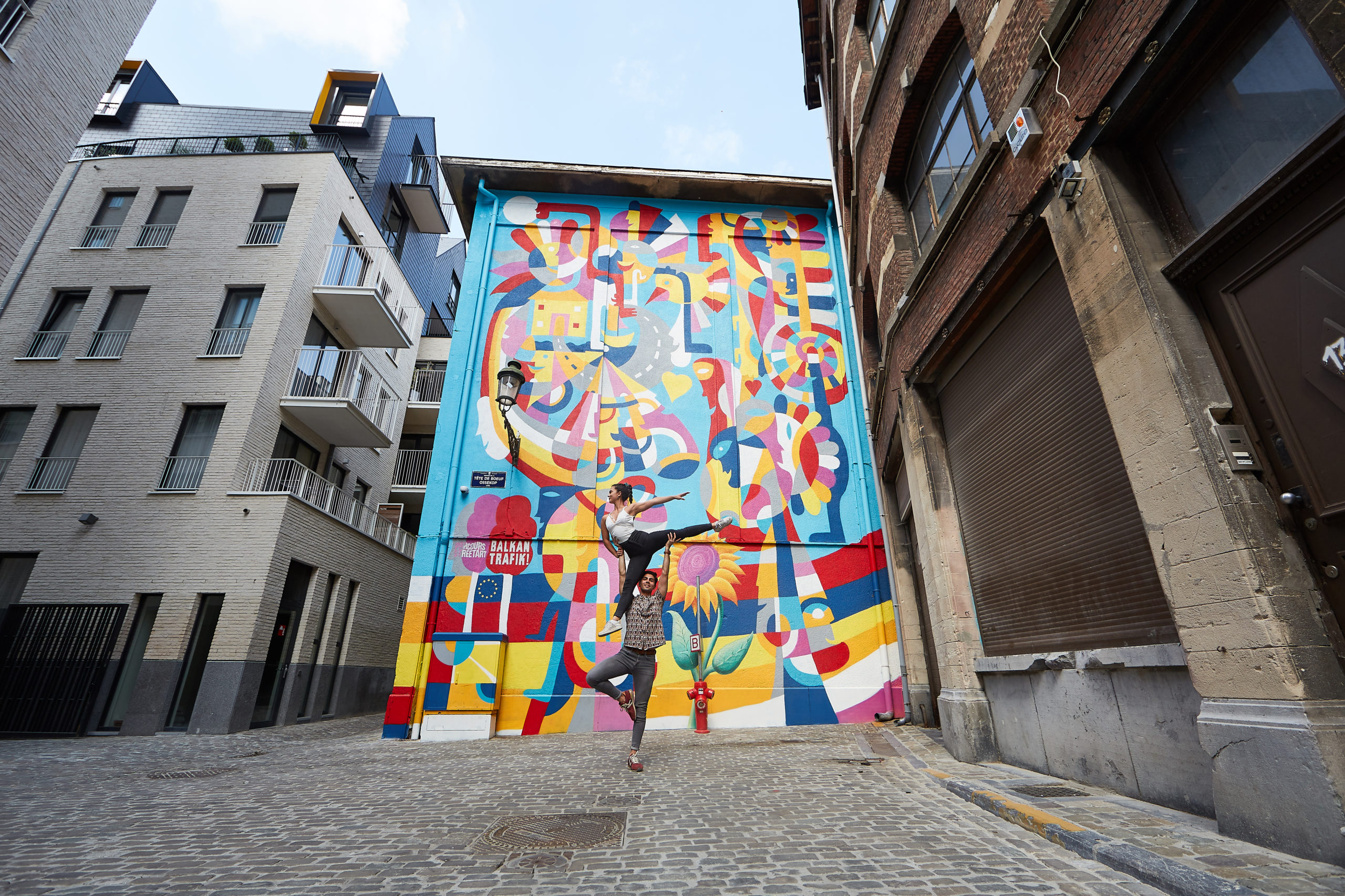 Deux jeunes adolescents effectuant une figure en pleine rue devant un mur très coloré