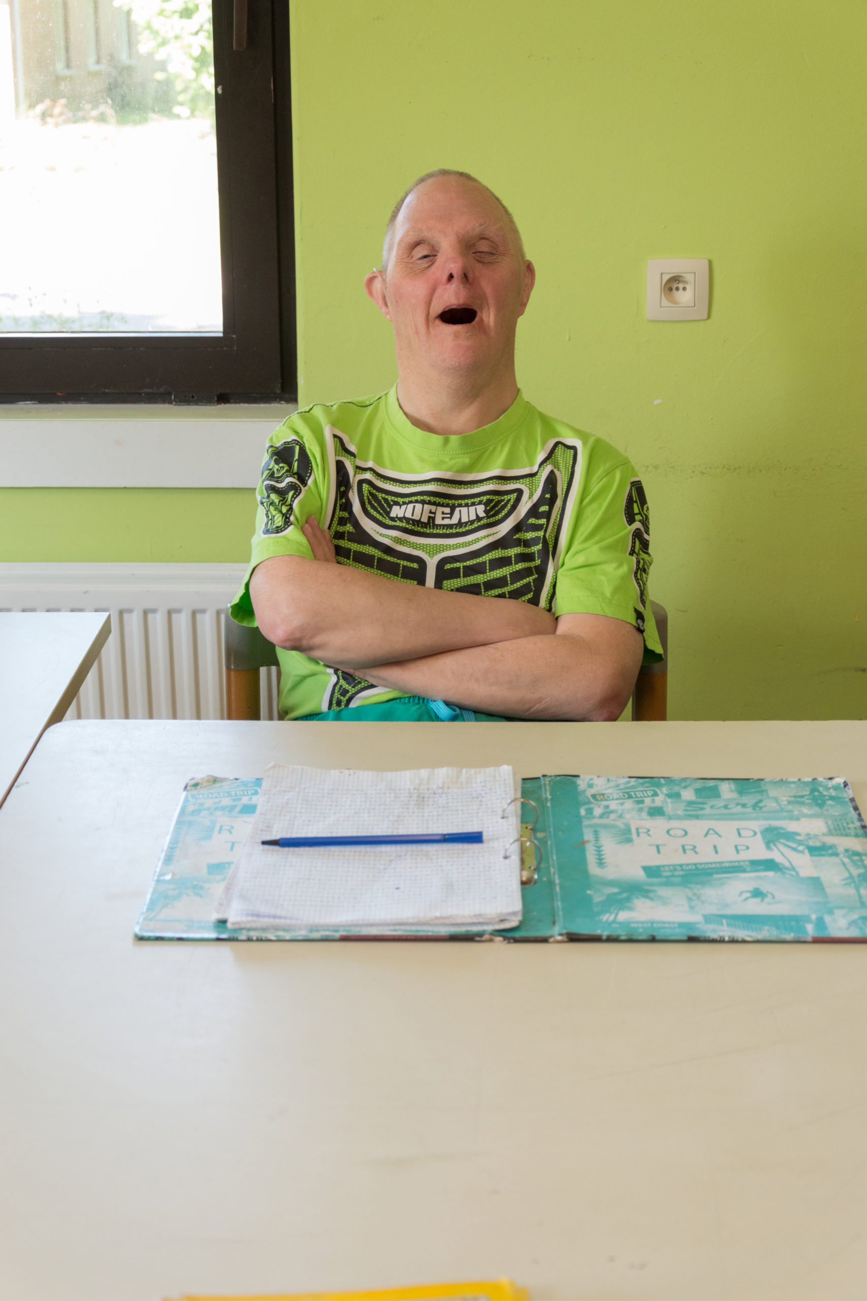 Homme handicapé qui souris assis à une table dans une pièce au mu vert avec une farde ouverte devant lui