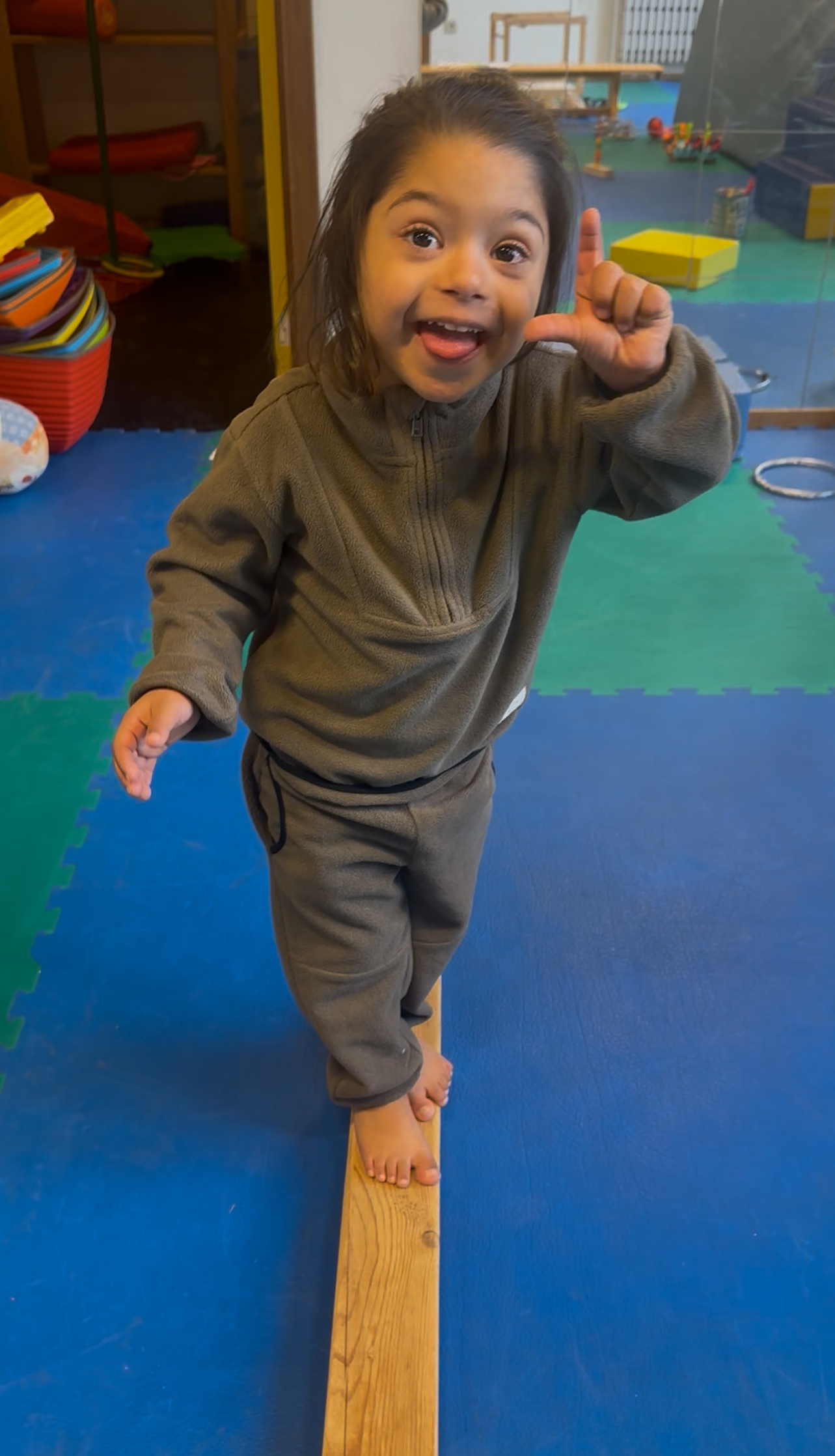 Photo d'un enfant suivi par le centre Étoile Polaire. L'enfant a un visage très expressif et fait un signe de la main. Il fait un exercice de psychomotricité sur une poutre.